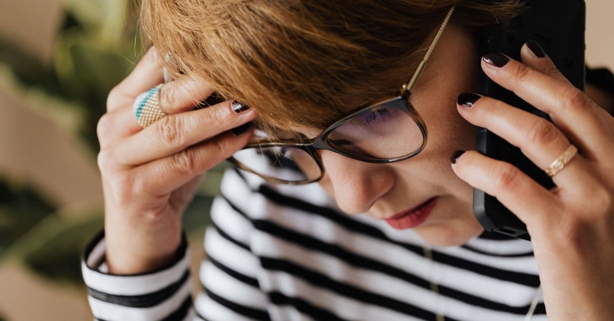 Crop upset adult female manager in eyeglasses feeling sad while having phone discussion during work in office