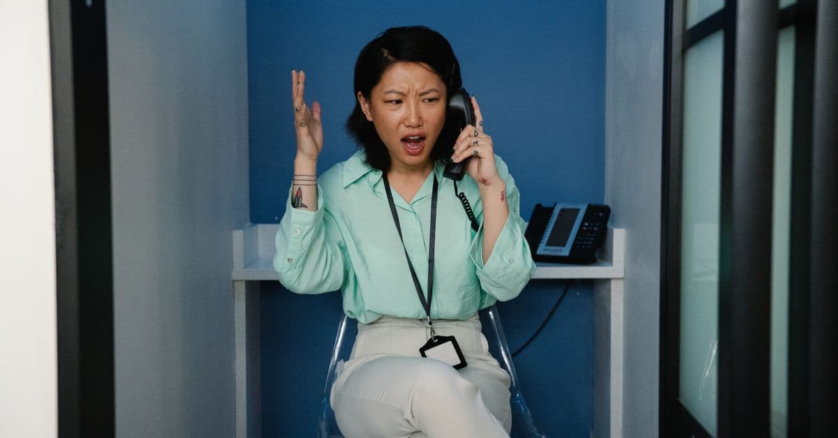 An east Asian woman expressing frustration during a phone call at the workplace.