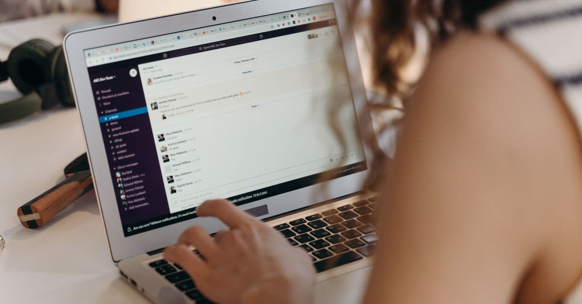 A businesswoman typing on a laptop in an office setting, using Slack for communication.
