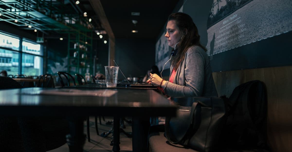 Focused woman using laptop with headphones in a cozy café setting.