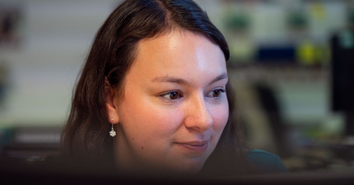 A professional woman concentrates on her computer screen in a busy office environment.