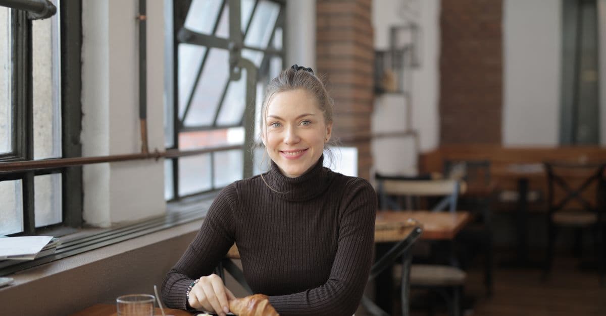 Woman enjoying a break with a croissant in a cozy indoor cafe setting.