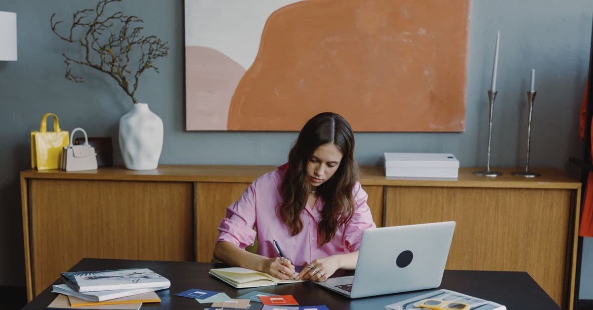 Woman working remotely at home office on a design project with laptop and color swatches.