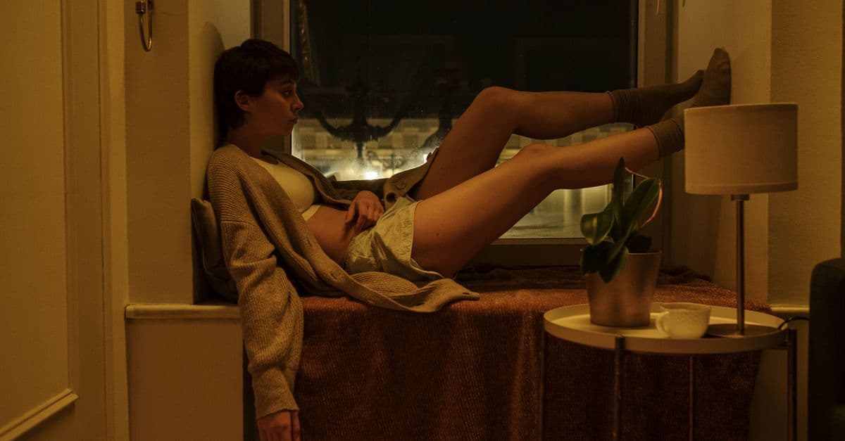 A woman sits by a window at night, exuding a vibe of tranquility and introspection.