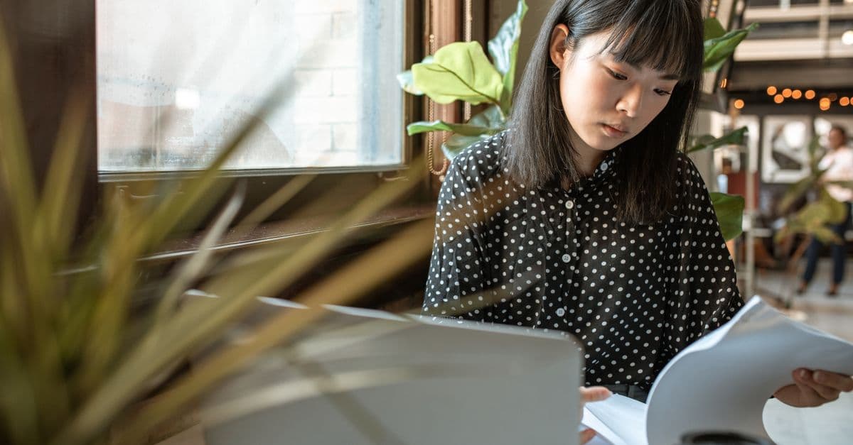 Asian woman intently working on documents at her laptop in a modern office setting.